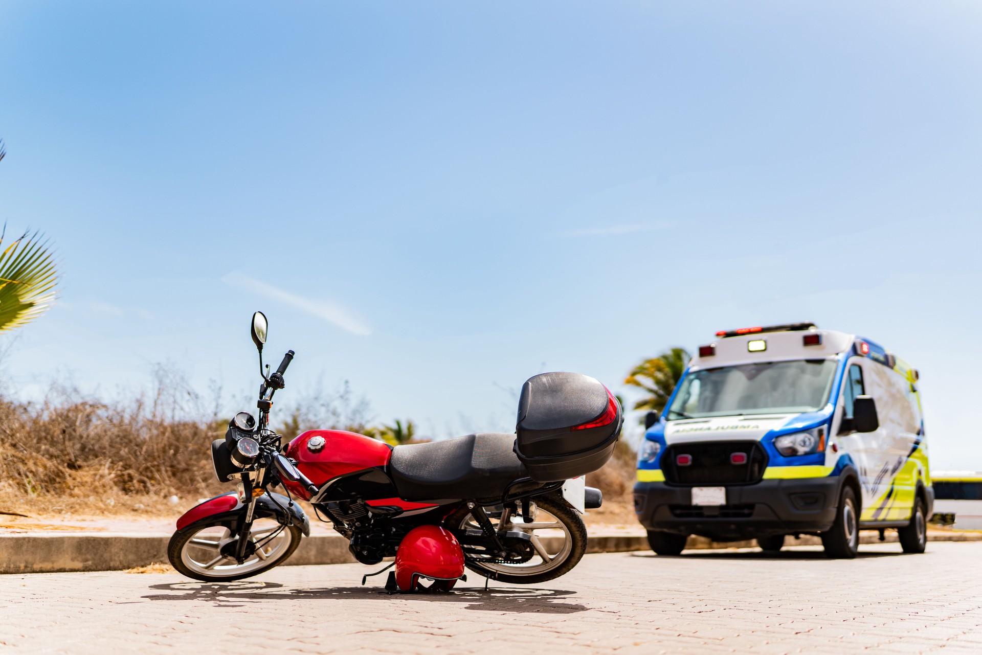 Red motorcycle lying on street after accident with ambulance in background