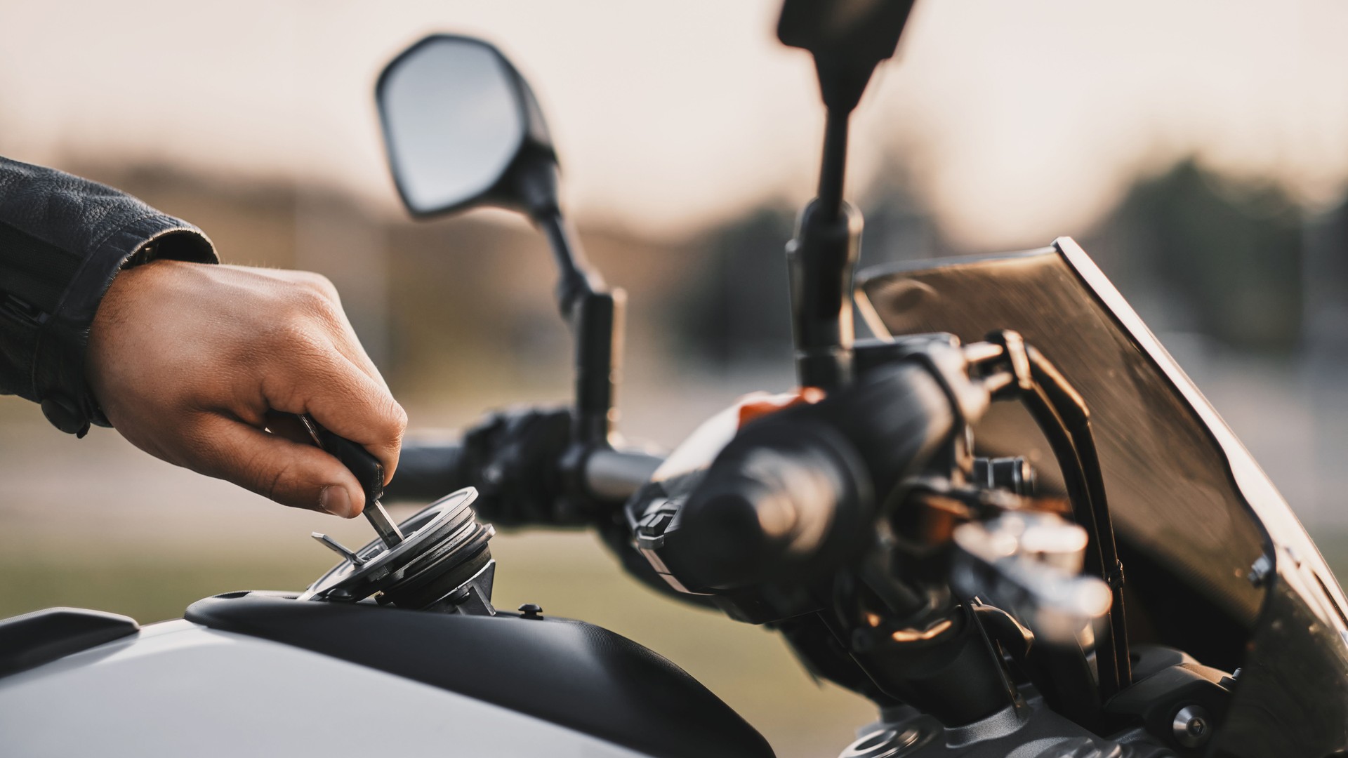 The motorcyclist opens the fuel tank cap while sitting on a motorcycle.